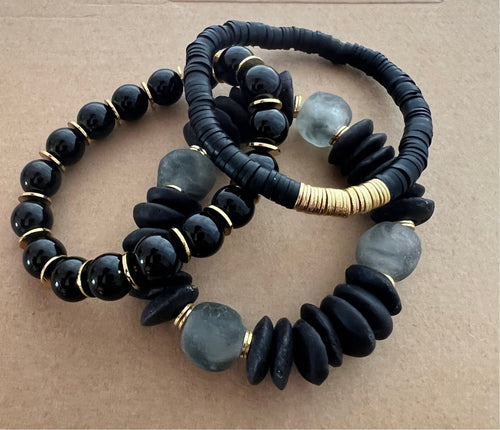 A very versatile black stack featuring a black ashanti glass bracelet with with grey recycled glass beads, and black polymer clay bracelet and a onyx bracelet with brushed gold accents  All bracelets measure 7 inches but can be customized upon request 
