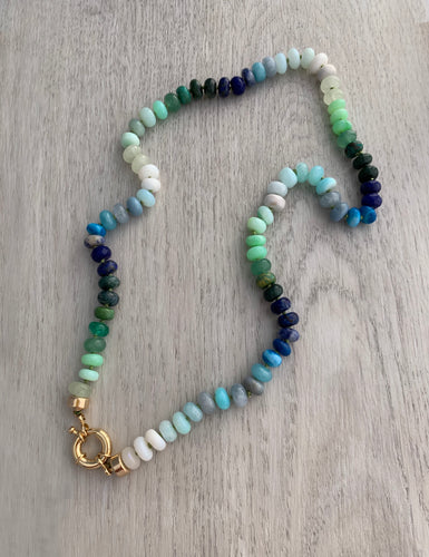 Hand knotted on white silk thread this multi color necklace features 8mm stones including moonstone, turquoise, aventurine, opals, lapis lazuli, and emerald. This necklace measures 21 inches and is finished off by a gold filled sailor clasp