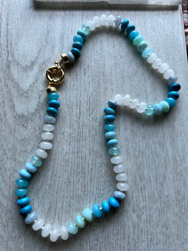 Hand knotted on blue silk this 19 inch necklace features a variety of natural smooth gemstones including moonstone, aquamarine, chalcedony and opals. Finished with a gold filled sailor clasp that allows you to easily put on and take off and add your favorite charm 