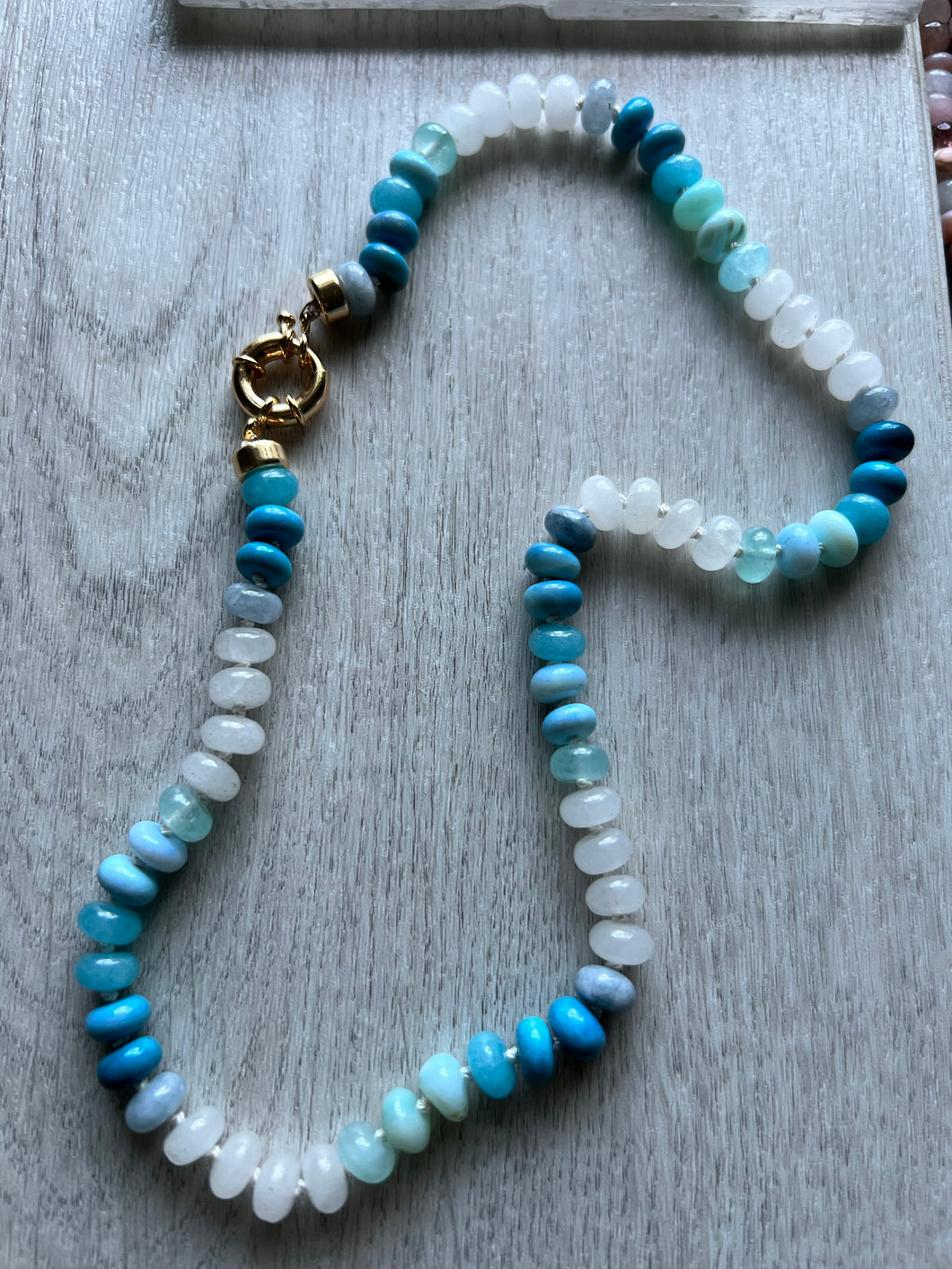 Hand knotted on blue silk this 19 inch necklace features a variety of natural smooth gemstones including moonstone, aquamarine, chalcedony and opals. Finished with a gold filled sailor clasp that allows you to easily put on and take off and add your favorite charm 